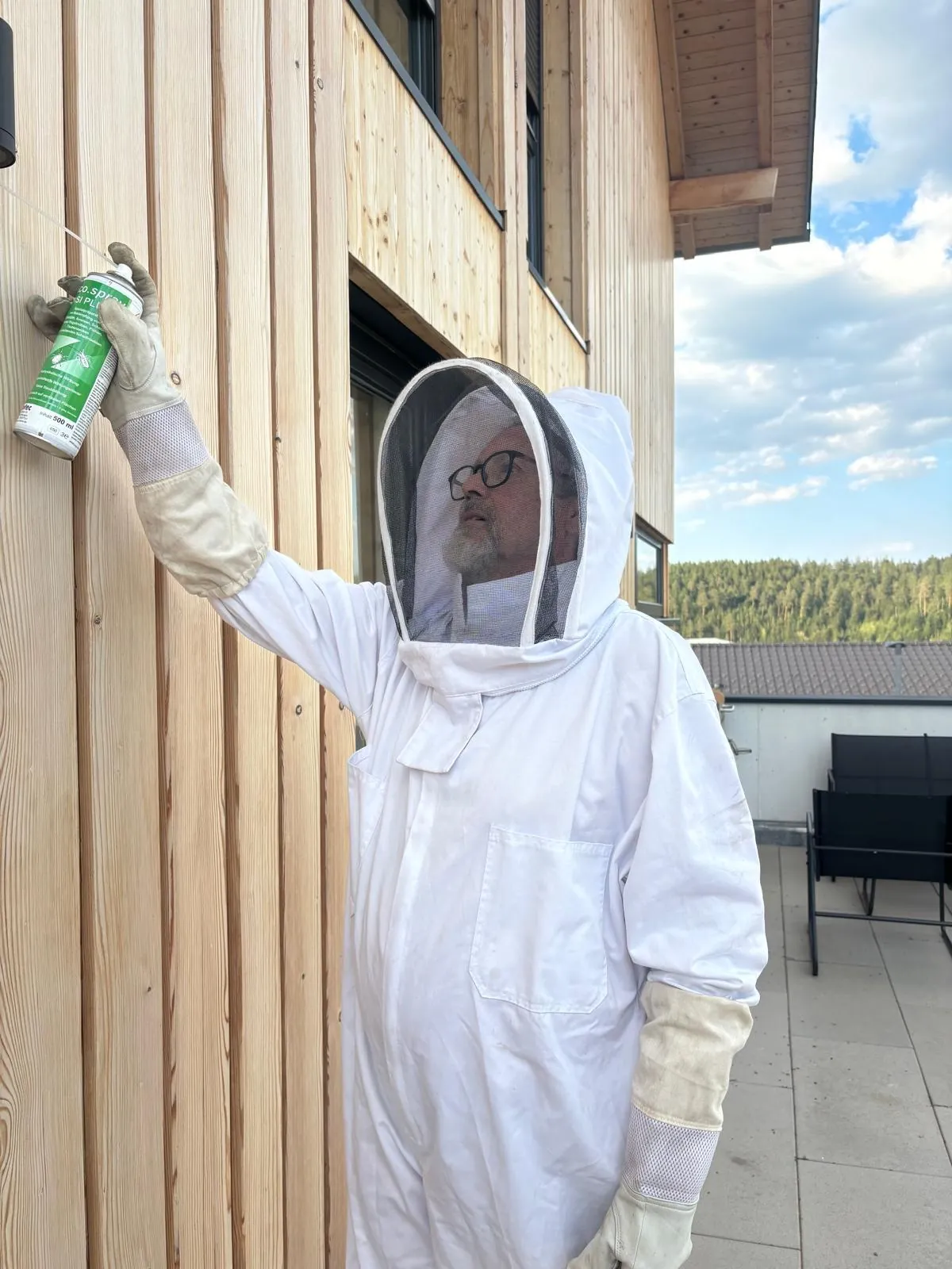 Schädlingsbekämpfer in Schutzanzug behandelt ein Wespennest an der Fassade